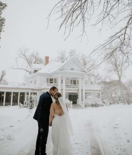 Couple kissing in front of the Norland, an estate wedding venue in Alberta, covered in snow during winter